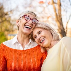 two mature women standing outside heads affectionately resting into one another