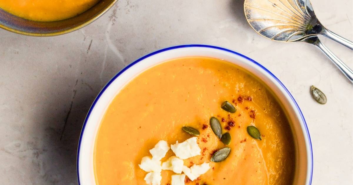 bowl of vibrant orange pumpkin soup in white bowl decorated with pumpkin seeds