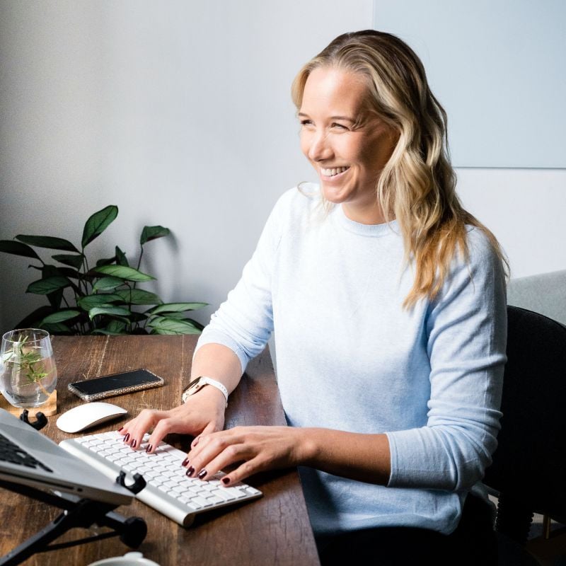 melbourne-functional-medicine-contact-form jessica cairns health coach sitting at desk smiling typing on computer