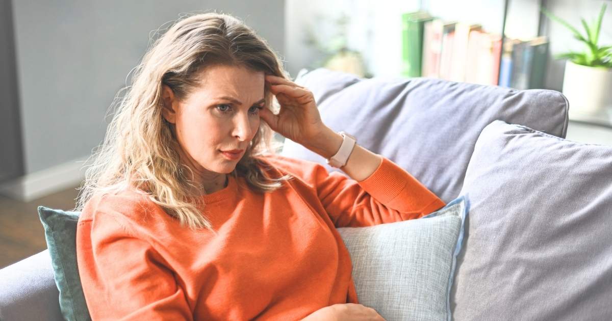 woman in midlife sitting on couch with hand to forehead looking concerned