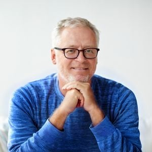 man wearing glasses gentle smile hands clasped under chin