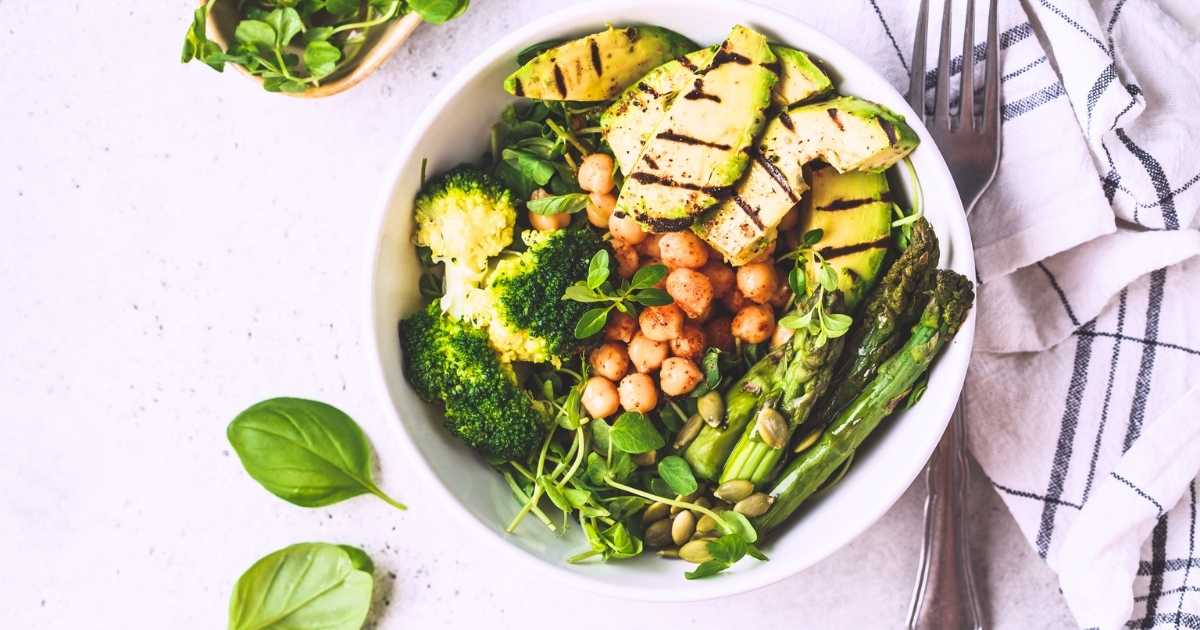 white bowl filled with broccoli avocado chickpeas pepitas spinach displayed on marble benchtop