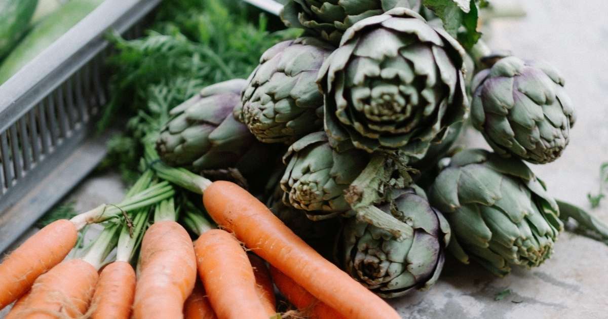 bunch of organic dutch carrots and artichokes laid out on timber benchtop