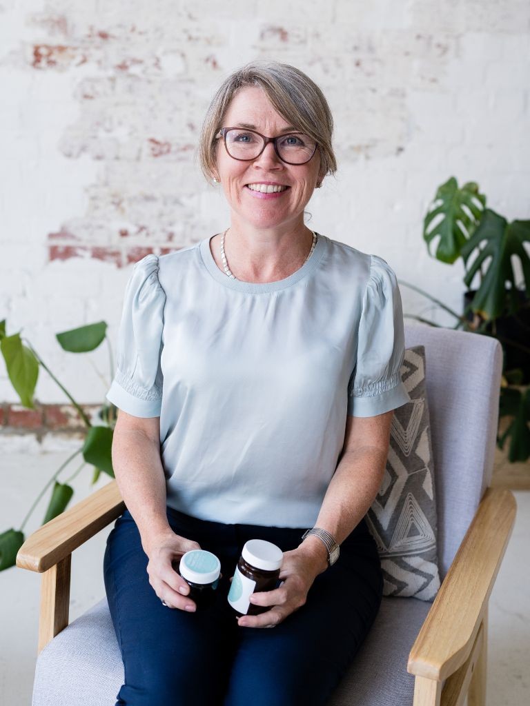 female functional medicine practitioner sitting in armchair smiling holding two jars of dispensary made topical cream