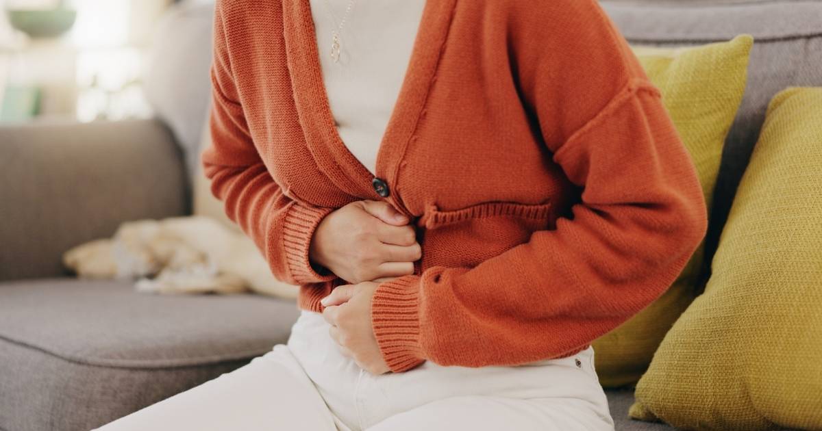 woman sitting on couch hands clenched around stomach