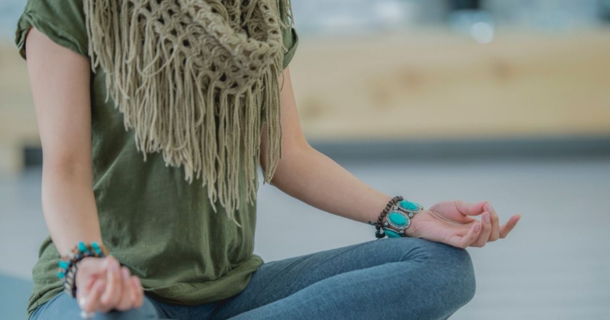 woman sitting crossed legged on floor in meditation position back of hands resting on knees