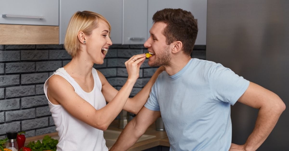young woman young man standing in kitchen woman putting piece sugary food into mans mouth