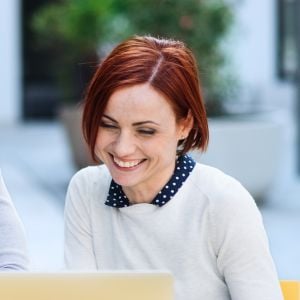 woman sitting at outdoor table looking at open laptop smiling