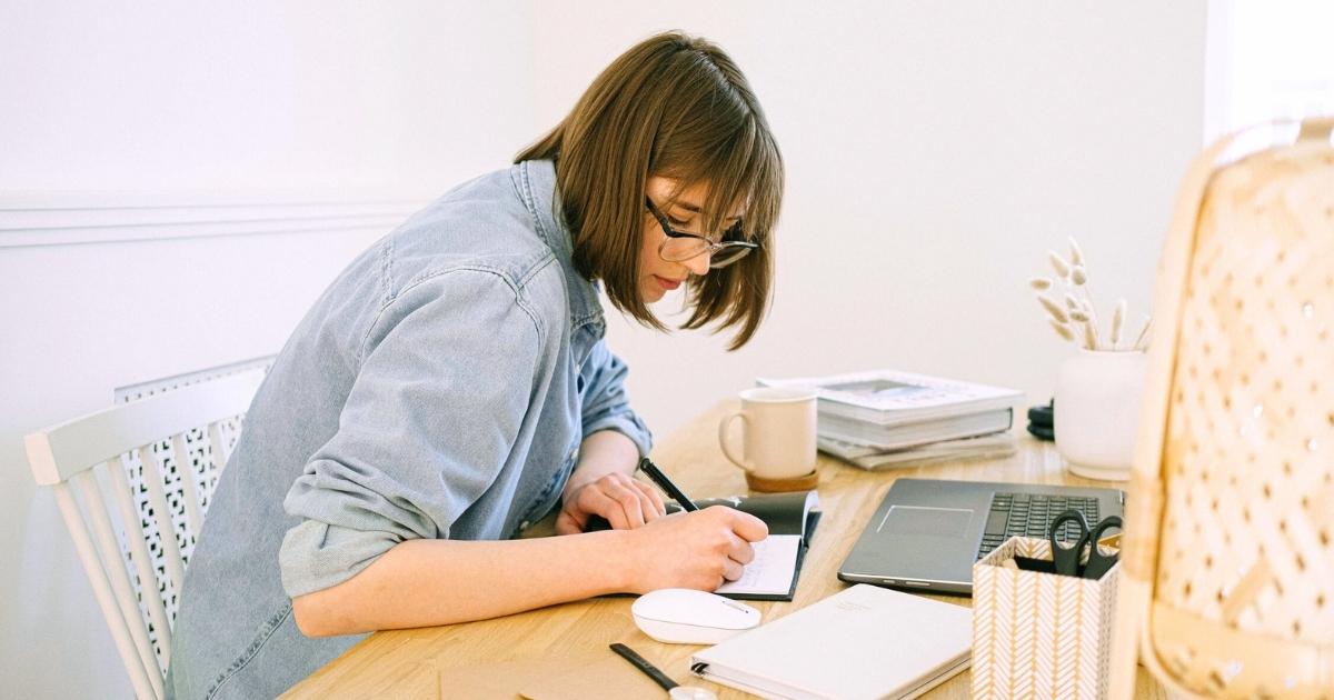 middle aged woman sitting at desk writing feelings emotions in journal